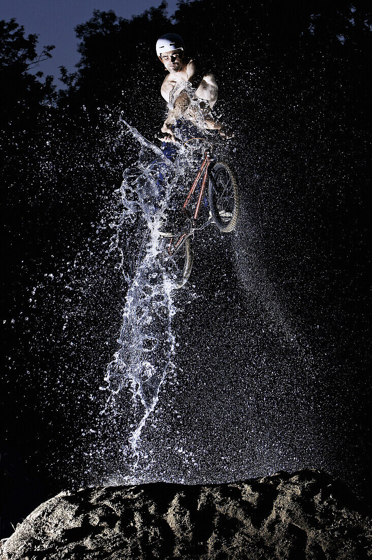 BMX bike rider jumping through water jet, Mindelheim, Bavaria, Germany