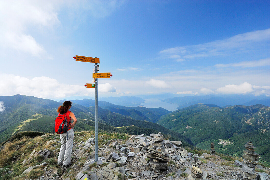 Frau auf Gipfel von Monte Tamaro mit Wegweiser und Steinmännern, Lago Maggiore im Hintergrund, Tessiner Alpen, Tessin, Schweiz