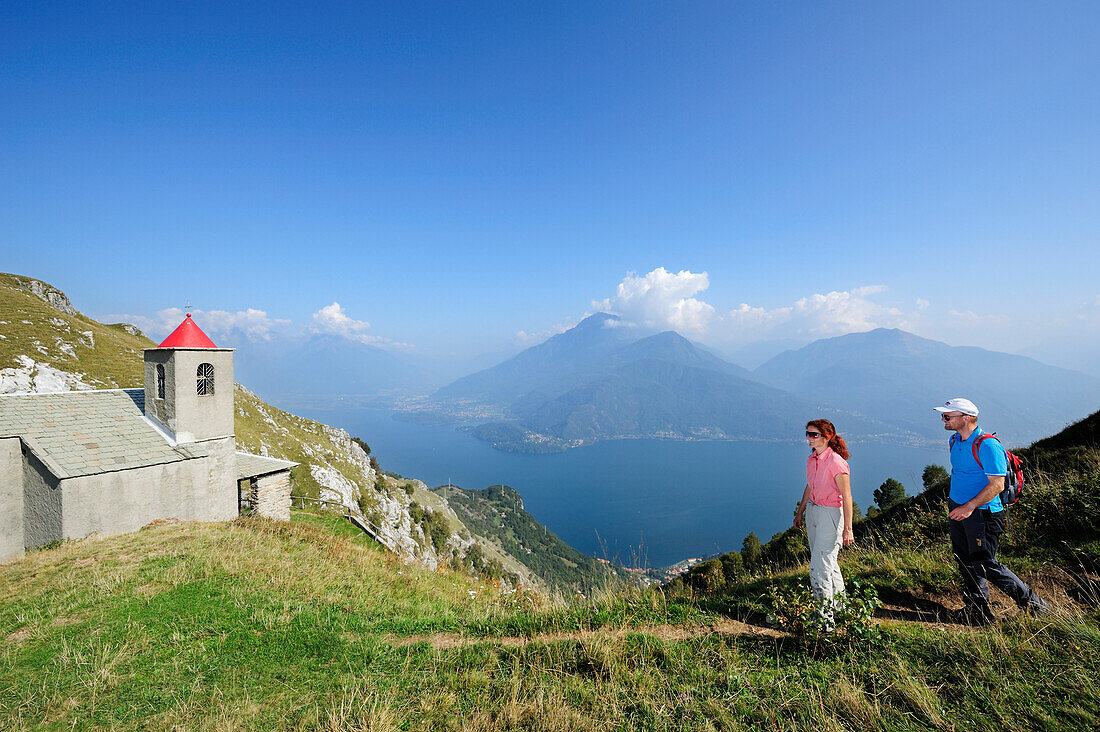 Two hikers near San Bernardo chapel, Monti Lariani, Lake Como in background, Lombardy, Italy
