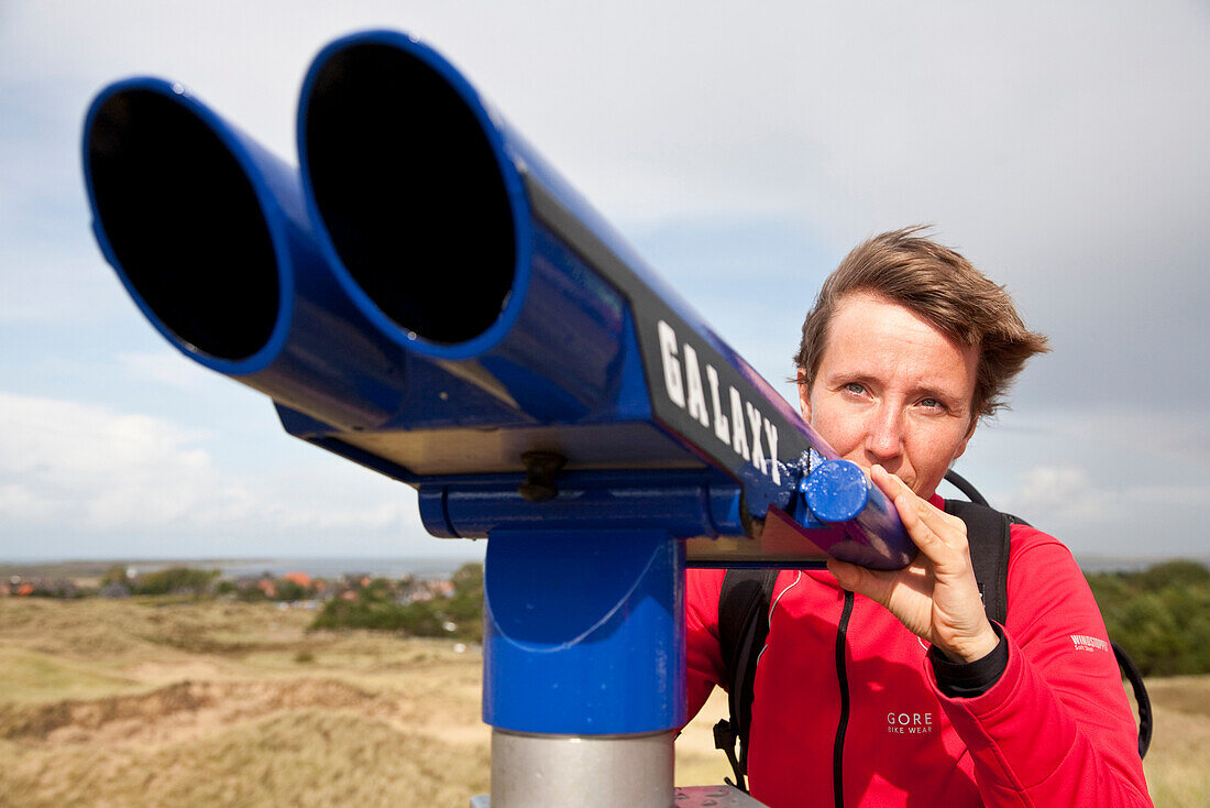 Woman looking through coin-operated binoculars over dunes, Norddorf, Amrum island, Schleswig-Holstein, Germany