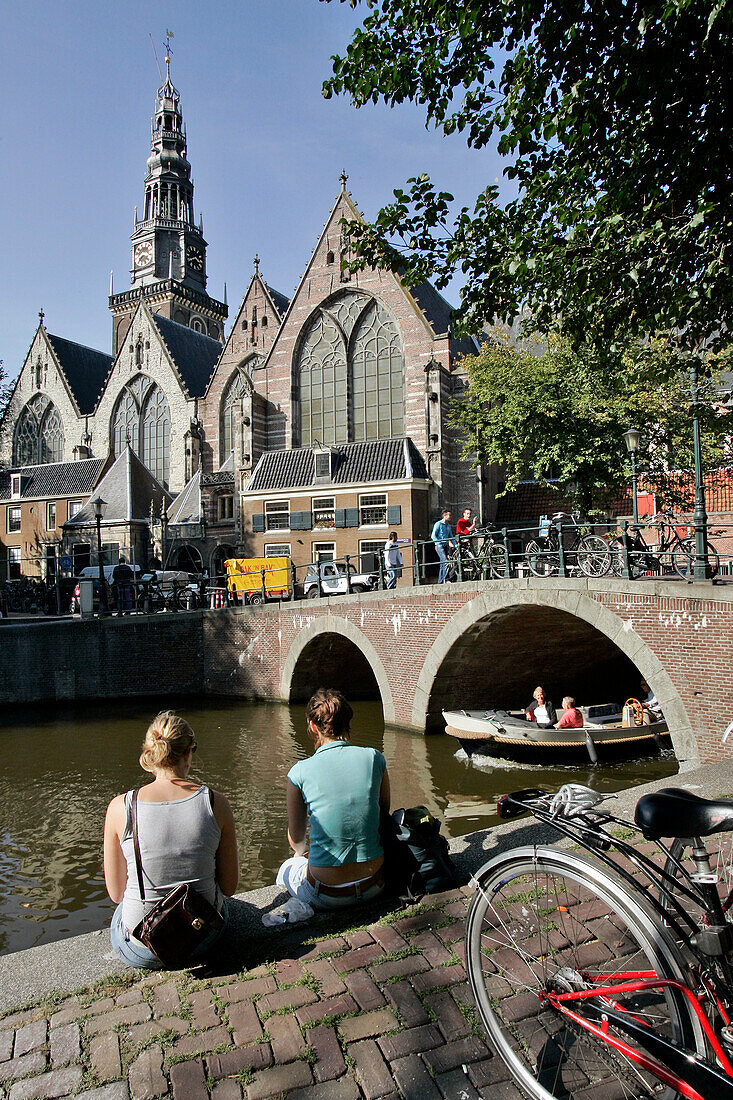 Relaxing On The Banks Of A Canal In Front Of The 'Oude Kerk' Church, Red Light District, Amsterdam, Netherlands