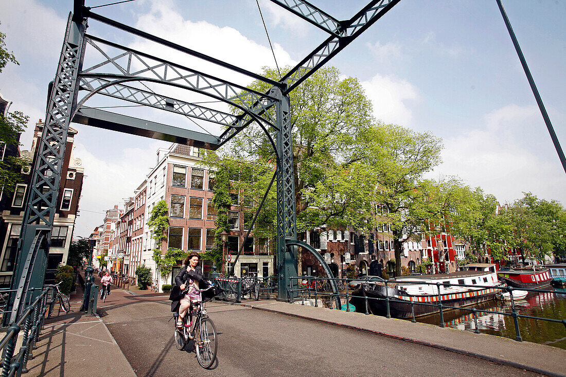 Woman Riding A Dutch Bike On A Bridge, Houseboat At The Quay Of A Canal And Facade Of A Traditional House, Amsterdam, Netherlands, Holland