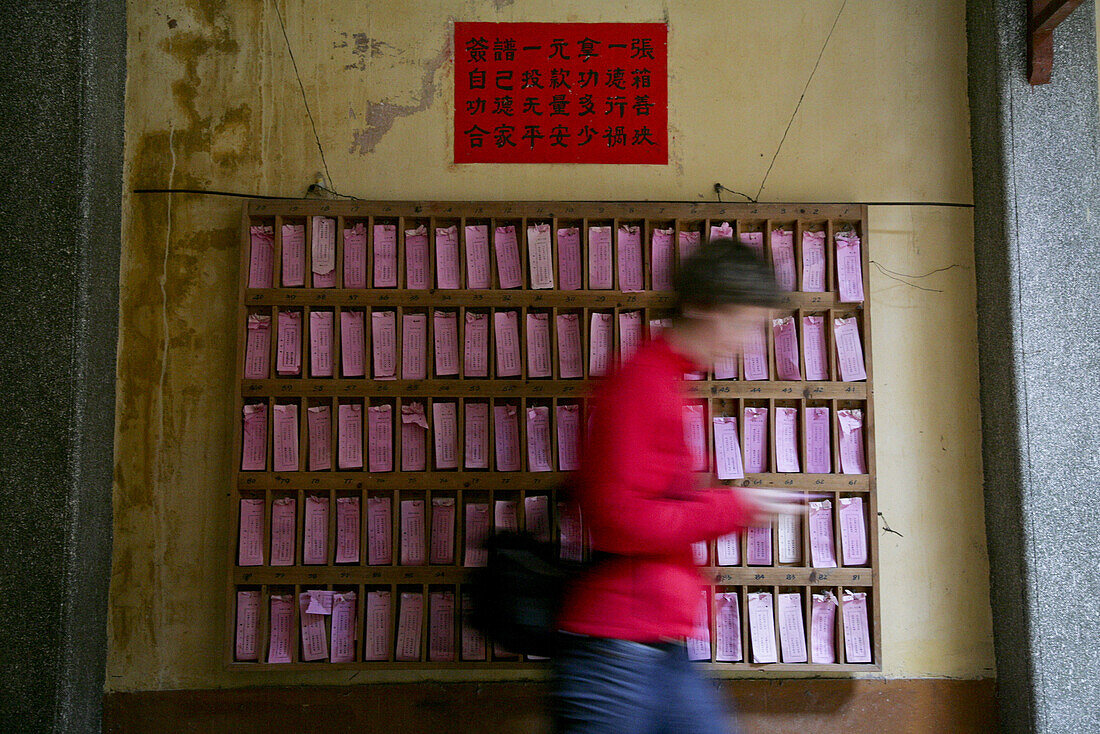 Buddhist temple, European woman passing a shelf with pink paper notes with religious sayings, Jinfeng, Changle, Fujian, China, Asia