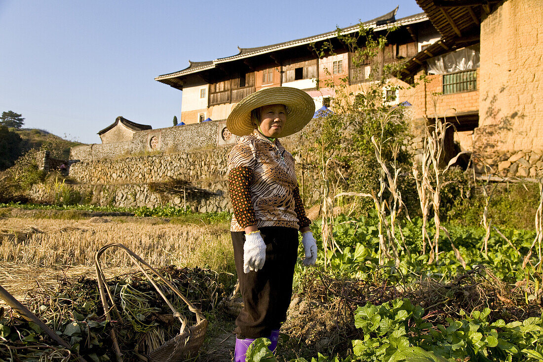 Chinese farmer on a field in front of traditional earthen house of the Hakka, Hongkeng, Longyan, Fujian, China, Asia
