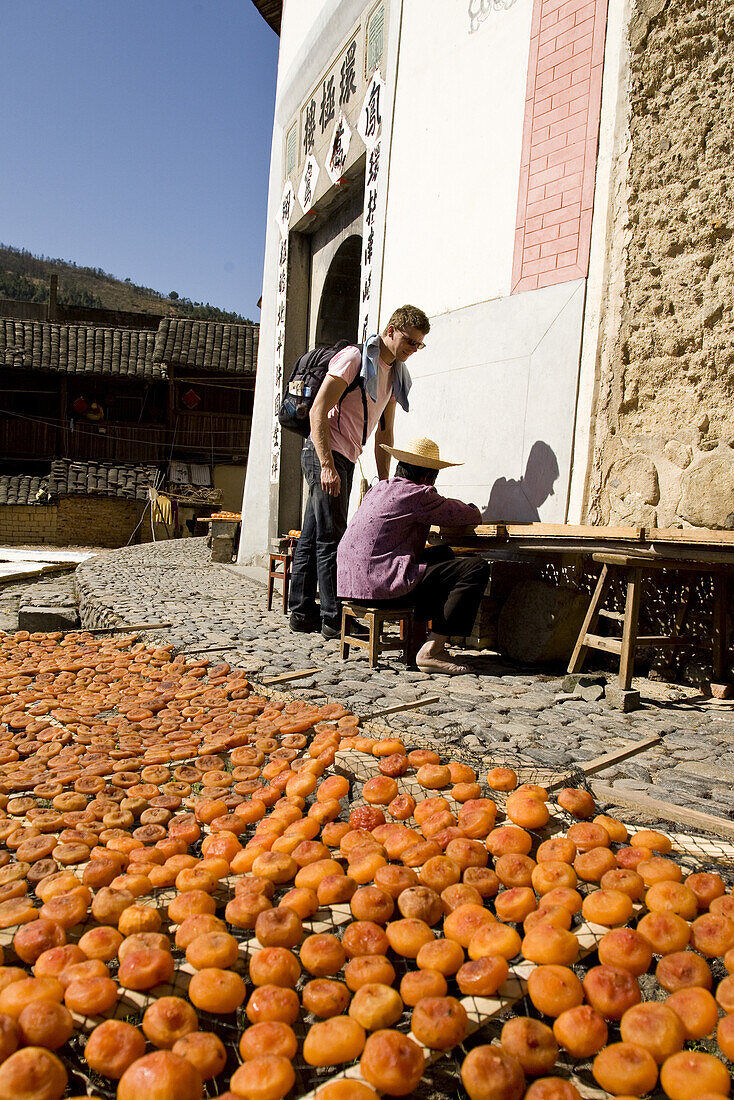 Tourist und chinesische Bäuerin vor traditionellem Haus der Hakka, Früchte trocknen in der Sonne, Hongkeng, Longyan, Fujian, China, Asien