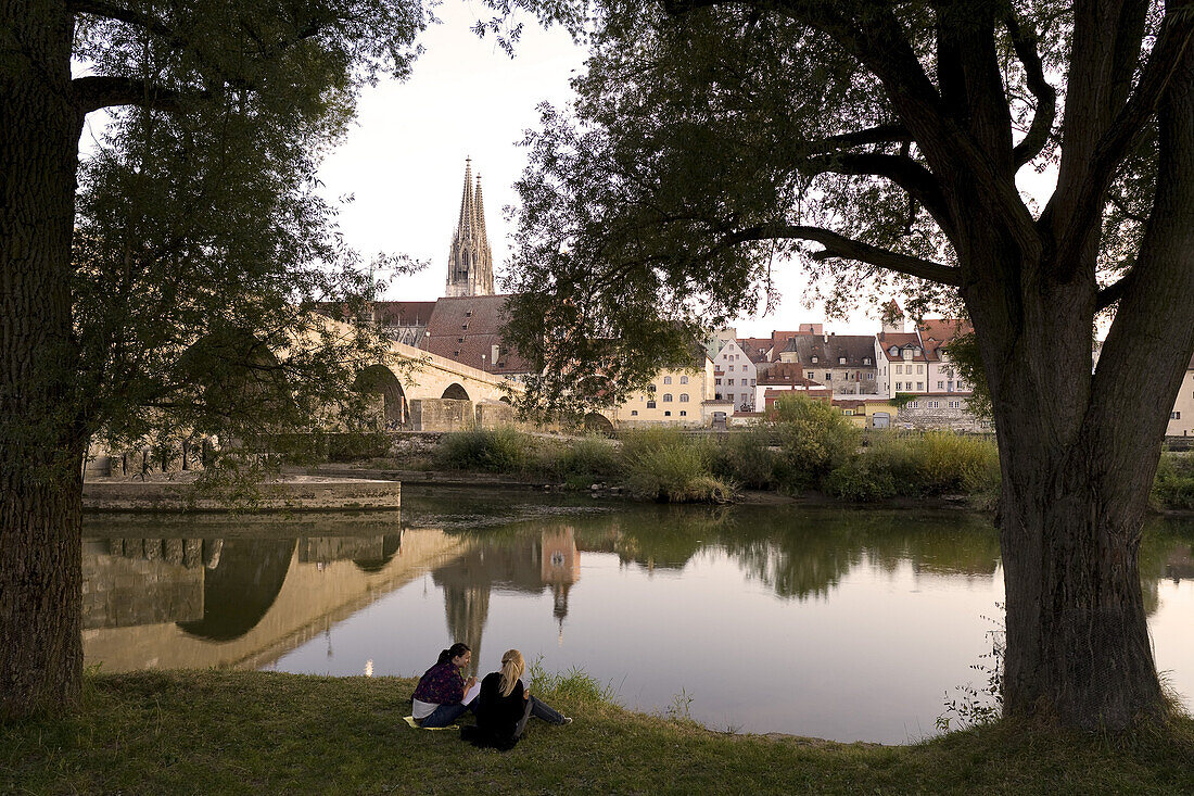 Zwei junge Frauen am Flußufer, Steinerne Brücke und Dom St. Peter, Regensburger Dom, Unesco-Weltkulturerbe, Donau, Regensburg, Oberpfalz, Ostbayern, Bayern, Deutschland, Europa