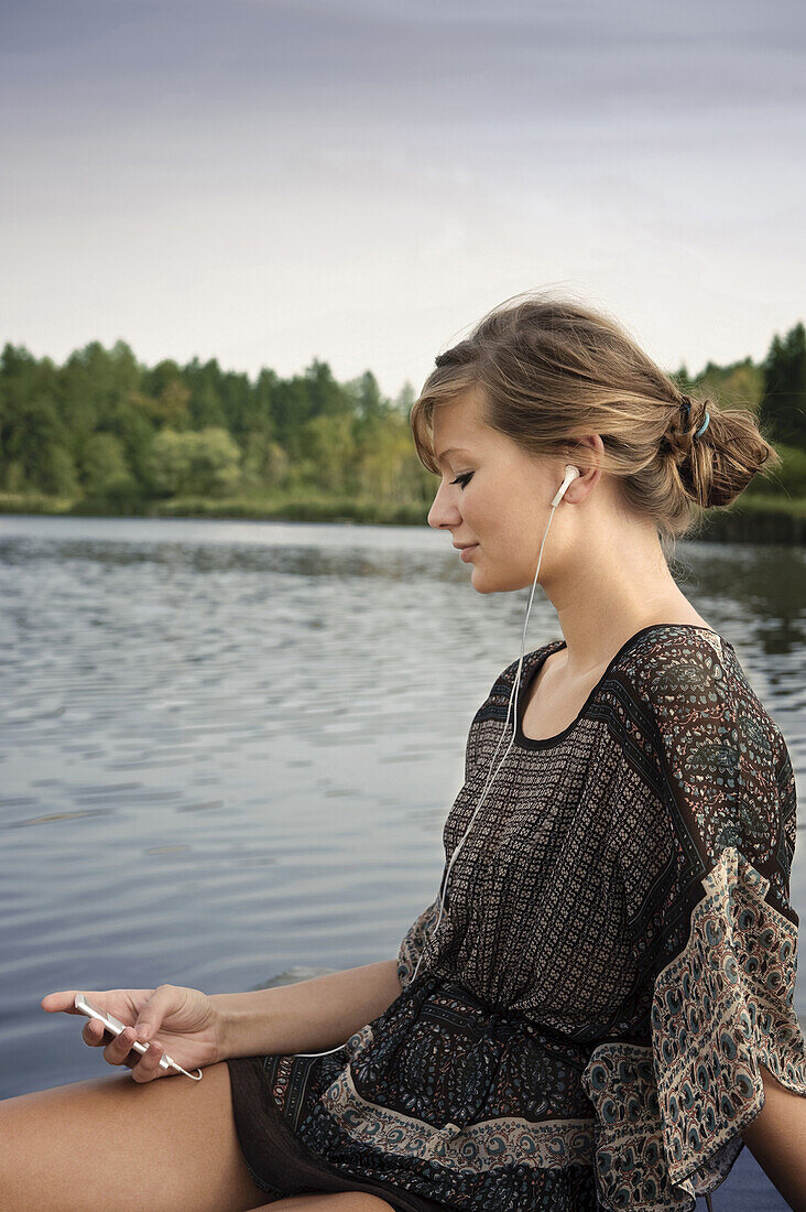 Junge Frau hört Musik am Starnberger See, Bayern, Deutschland