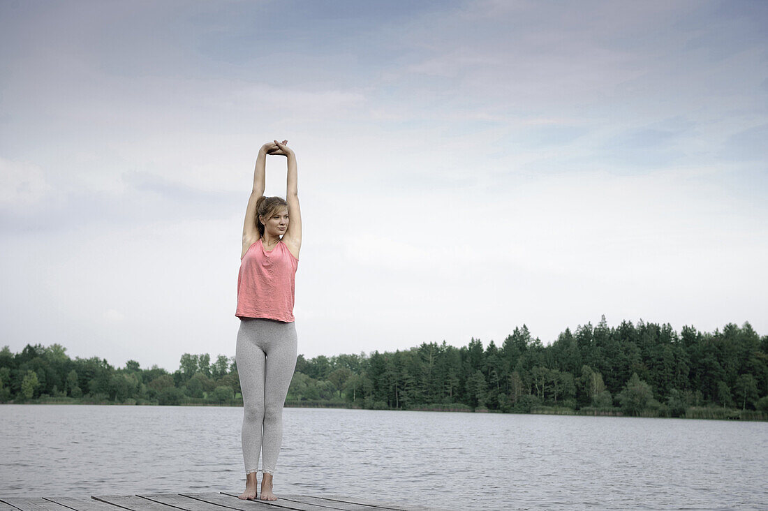 Young woman stretching on a jetty at lake Starnberg, Bavaria, Germany