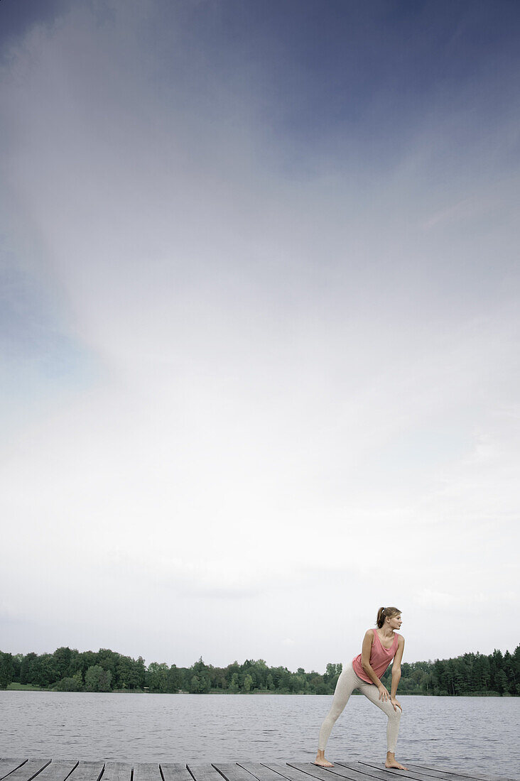 Junge Frau beim Stretching auf einem Steg am Starnberger See, Bayern, Deutschland