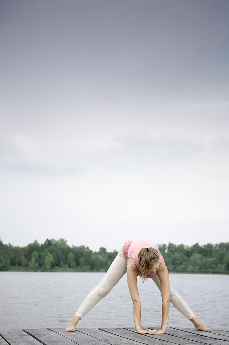 Young woman stretching on a jetty at lake Starnberg, Bavaria, Germany