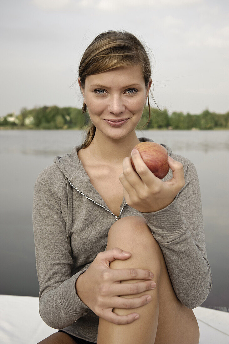 Young woman holding an apple, lake Starnberg, Bavaria, Germany