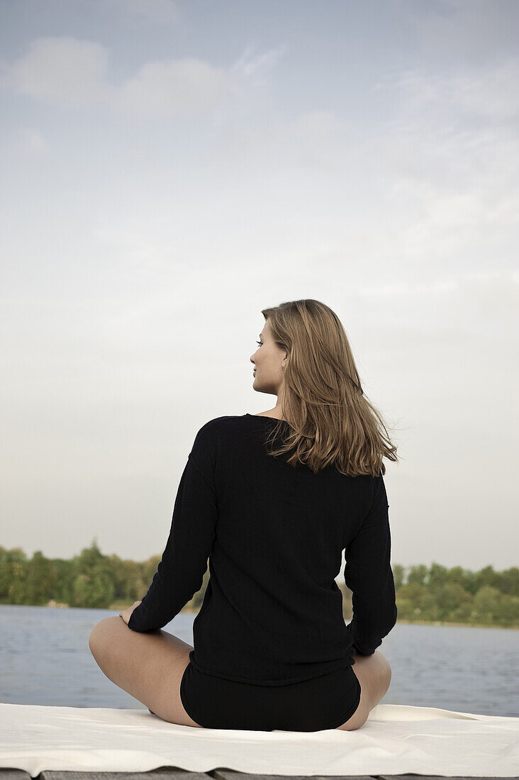 Young woman sitting on jetty at lake Starnberg, Bavaria, Germany