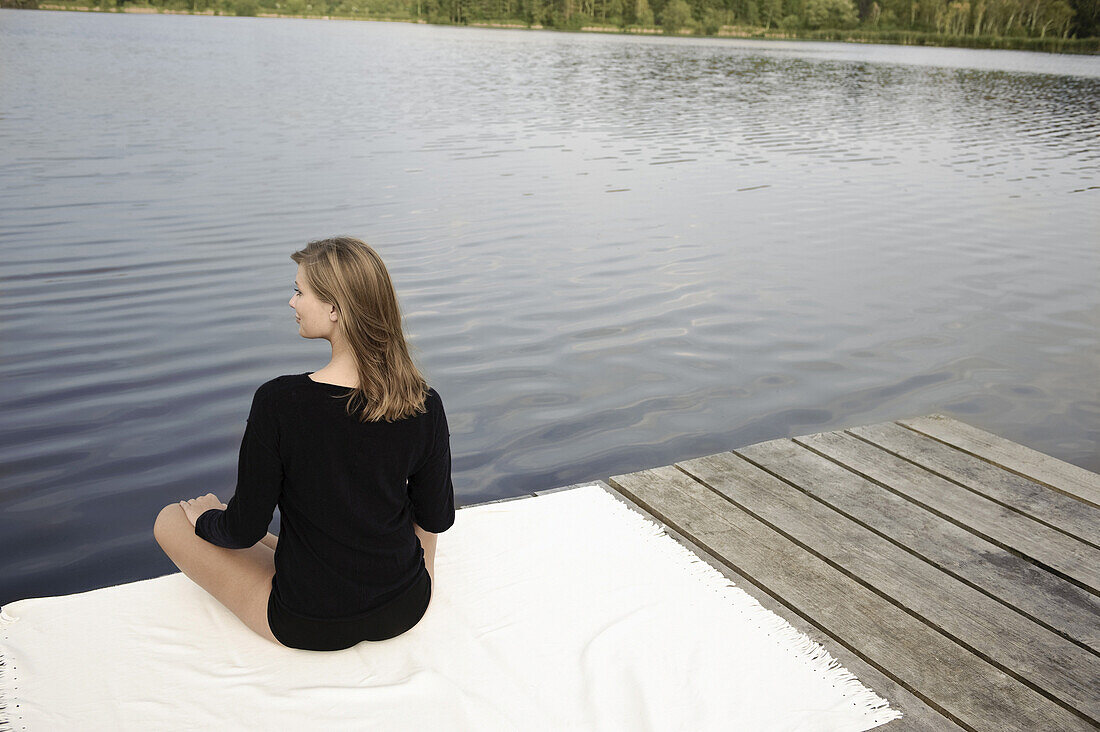Junge Frau sitzt auf einem Steg am Starnberger See, Bayern, Deutschland