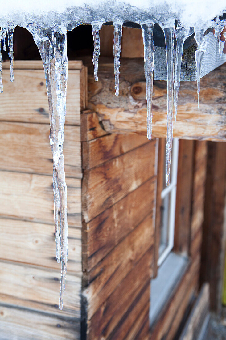 Eiszapfen am Dach einer Holzhütte