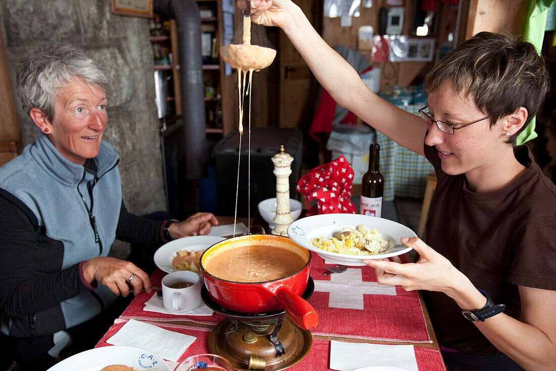 Two women enjoying tomato fondue, mountain lodge Cabane de l'A Neuve, Val Ferret, Canton of Valais, Switzerland