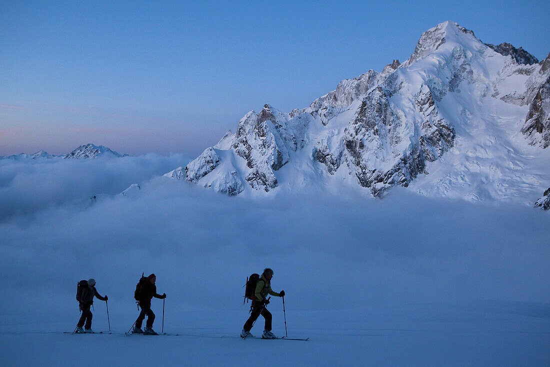 Three back-country skiers in morning mist, Val Ferret, Canton of Valais, Switzerland