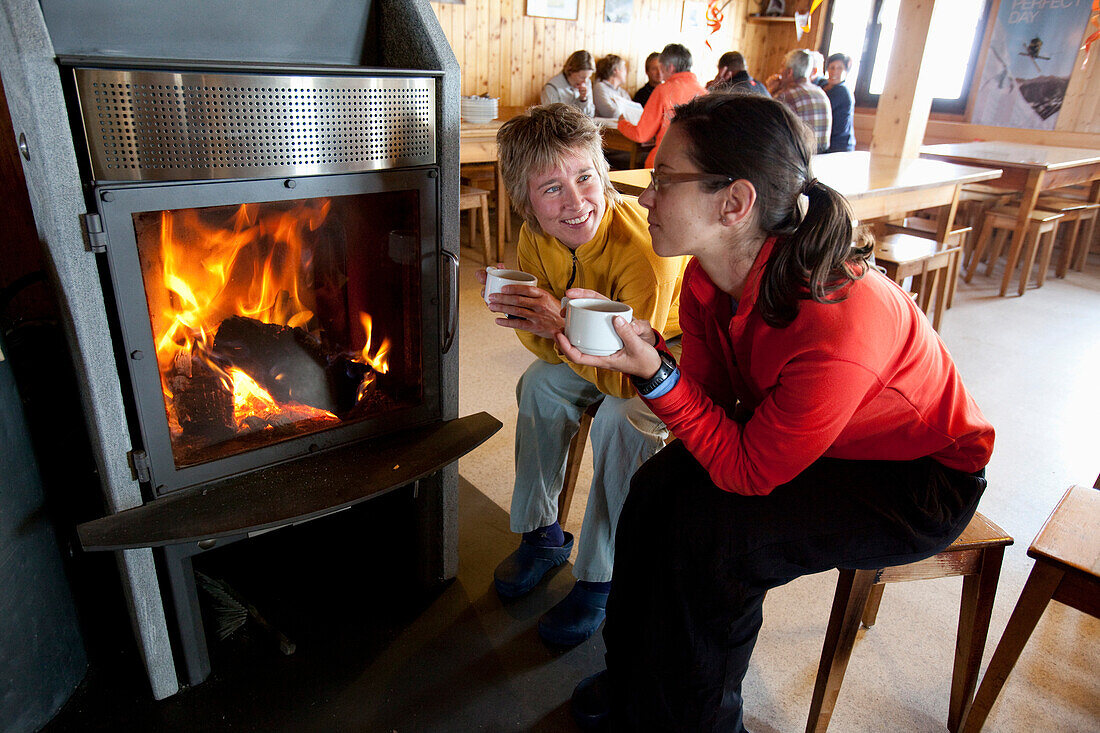 Two women sitting beside a fireplace inside Wildhorn mountain lodge, Bernese Oberland, Canton of Bern, Switzerland