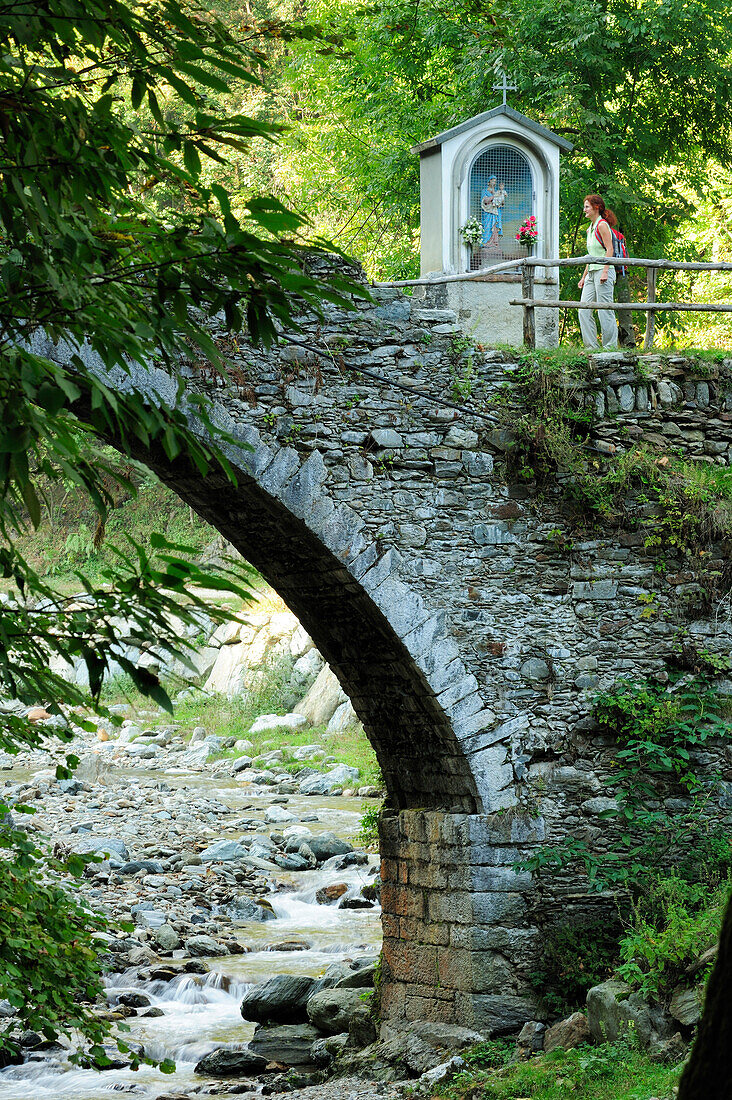 Woman passing stone bridge, Via Dei Monti Lariani, Lake Como, Ticino range, Lombardy, Italy