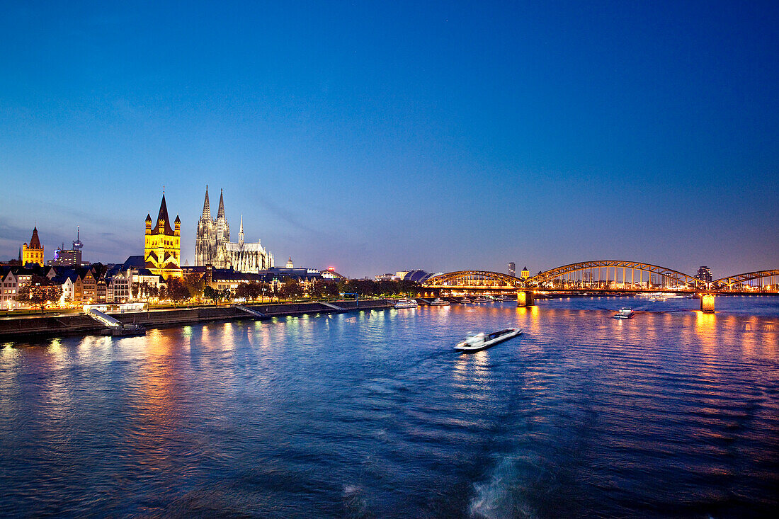 View over river Rhine to old town with cathedral and Great St. Martin church at night, Cologne, North Rhine-Westphalia, Germany