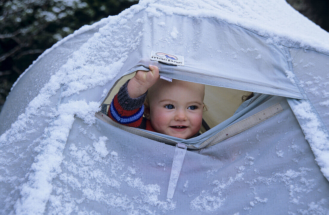 Child peering out of snow-covered tent Whitehorse Hill Aoraki /Mt Cook National Park New Zealand