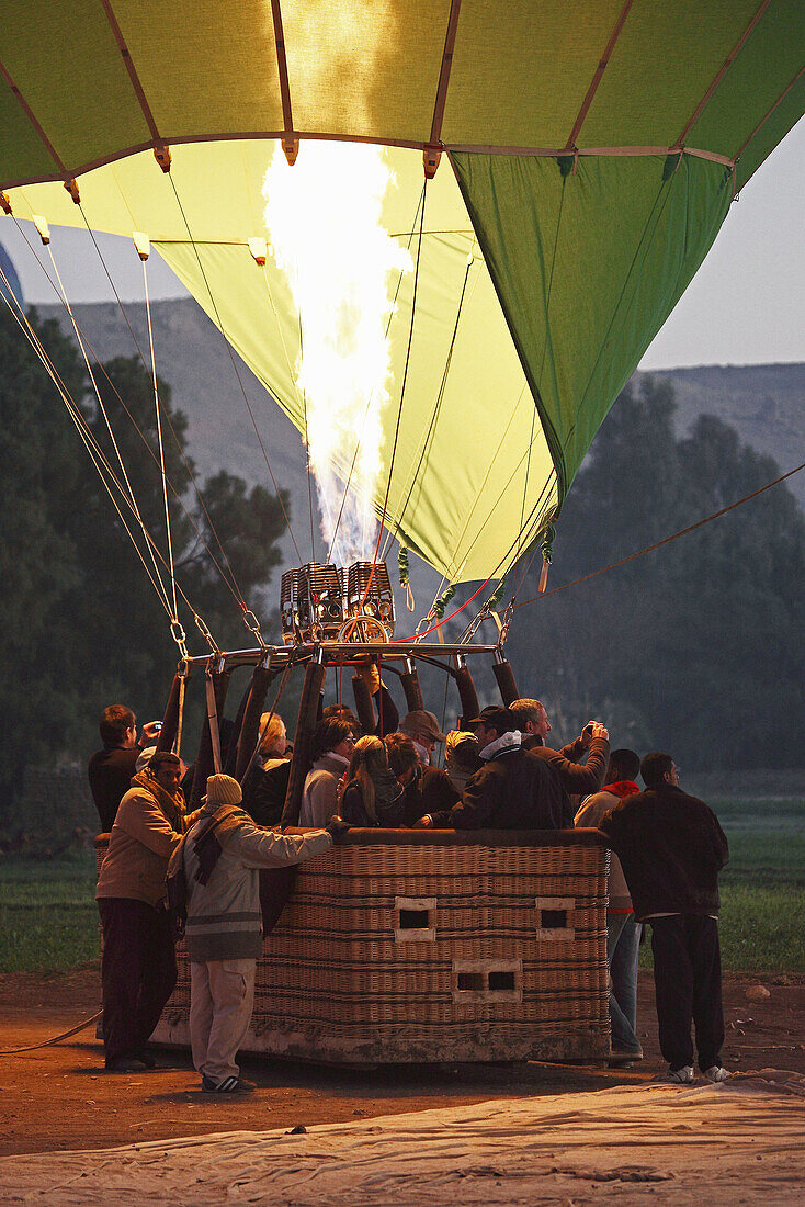 Hot air balloon,  jet of flame and passengers prepare to ascend at dawn over the Valley of the Kings and Queens,  Al Asasif,  Luxor,  Egypt,  Africa