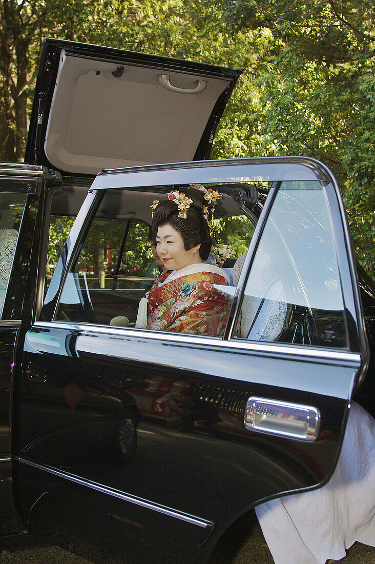 A just married Japanese bride and groom sitting in a special marriage taxi showing it´s special roof hatch opened to allow the bride with a high wedding hair style to get inside the taxi without trouble