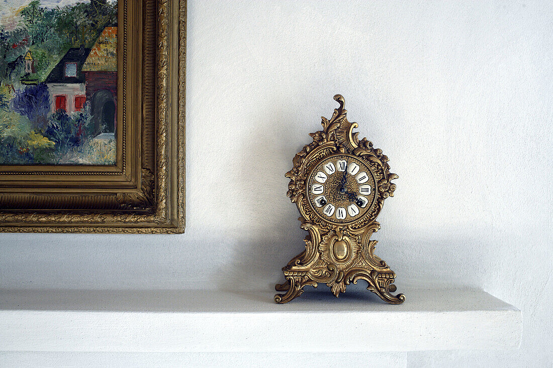 Old antique clock standing on the mantelpiece of a fire-place besides a colorful painting of the famous painter Monet,  Gabiano,  Piemont,  Italy,  Europe