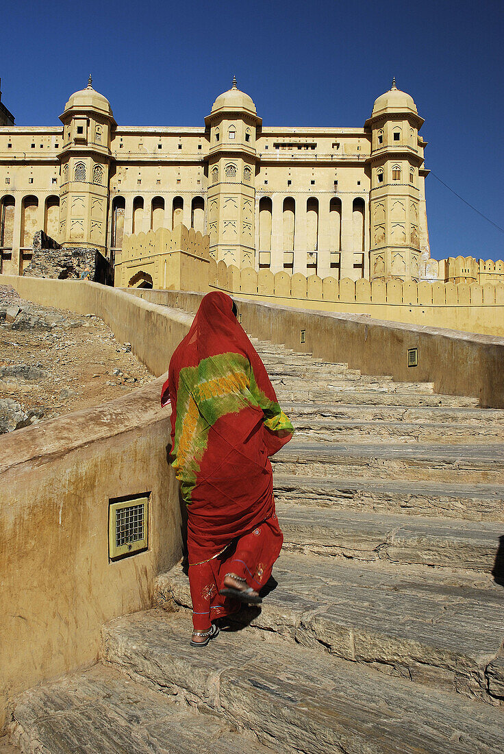 Woman in orange sari walking up to Amber Fort  Jaipur  India