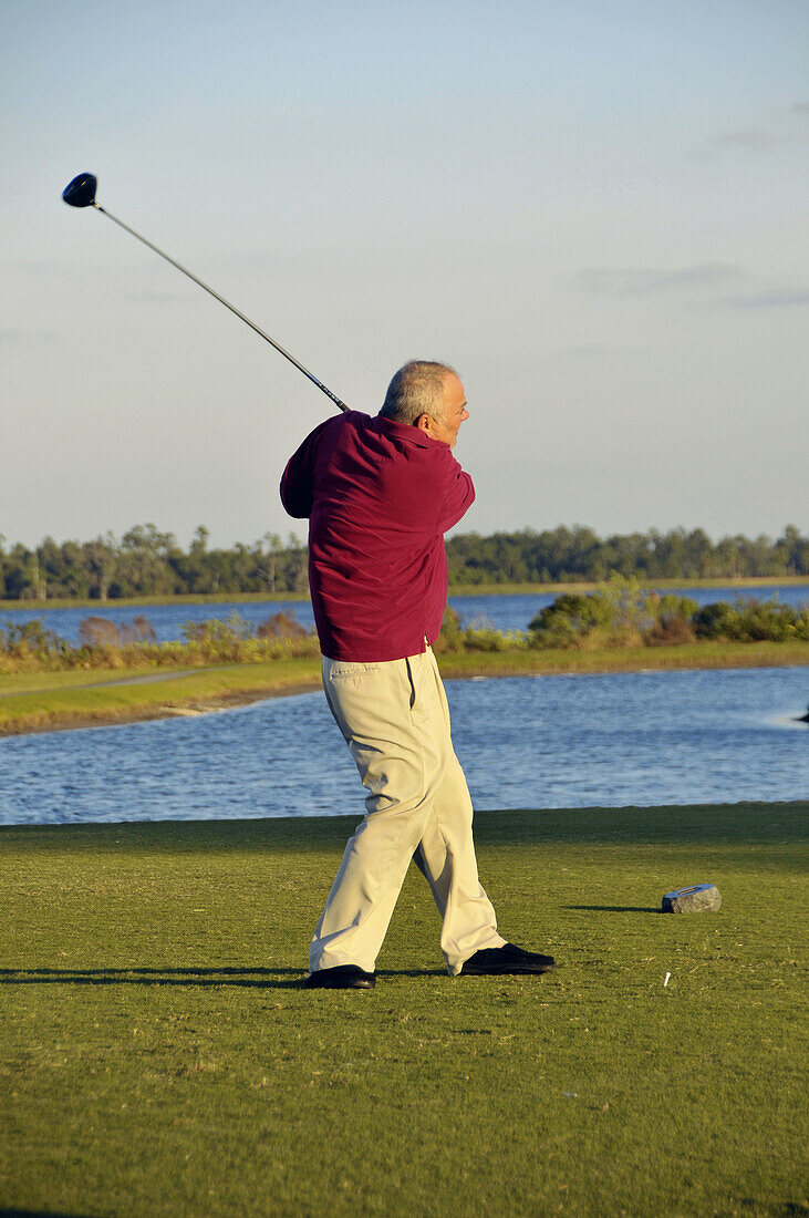 White Male Senior Citizen swings golf club on Florida golf course in retirement community