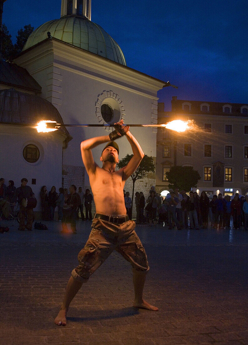 Street performer juggles sticks of fire at night,  Main Market Square,  Krakow,  Poland