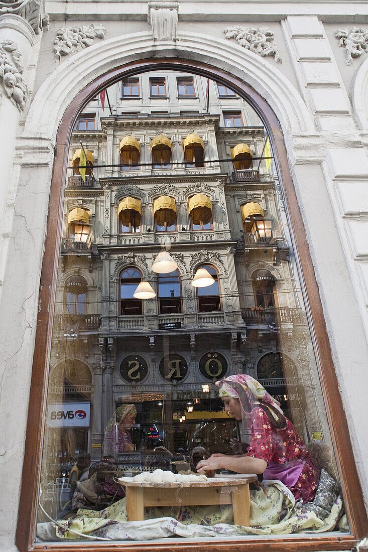 in einem Schaufenster eines traditionellen Restaurants formt eine Frau Teigtaschen, Spiegelung der gegenüberliegenden Fassade, Istiklal Caddesi, Unabhängigkeitsstraße, Istanbul