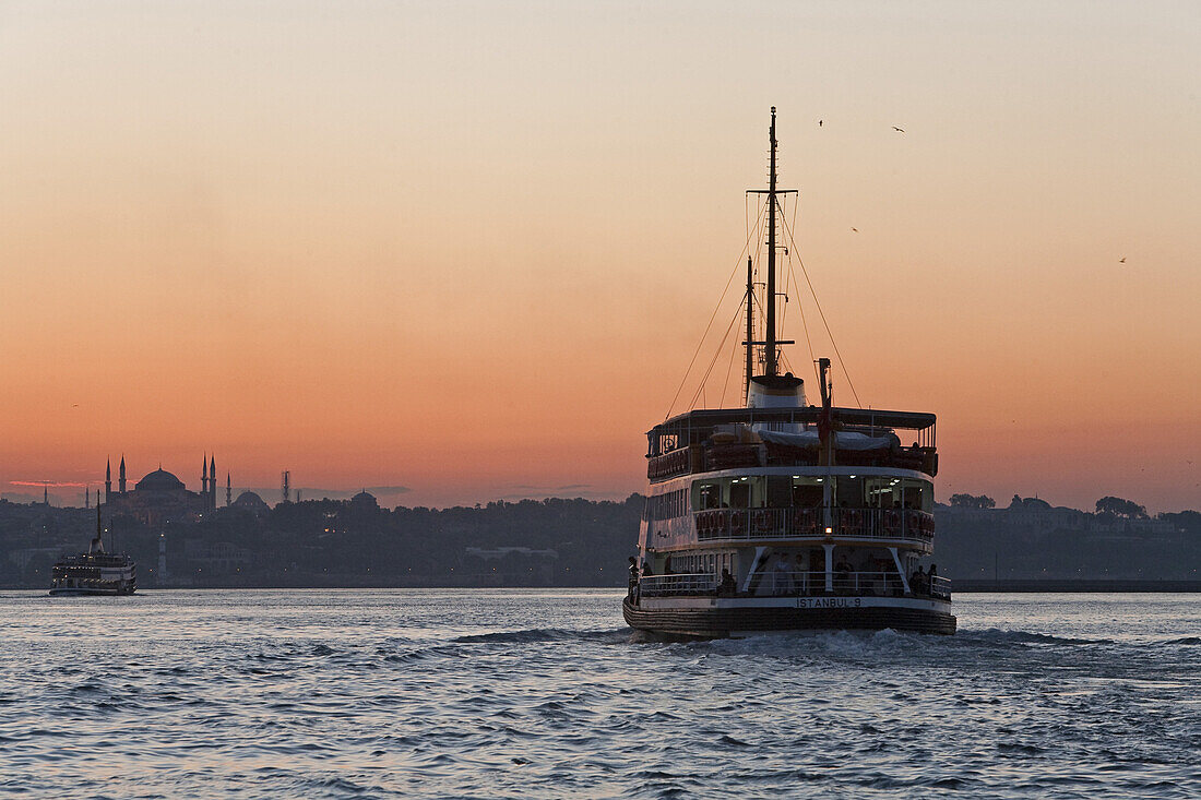Ferry across Golden Horn at sunset, city skyline in background with Hagia Sofia, Istanbul, Turkey