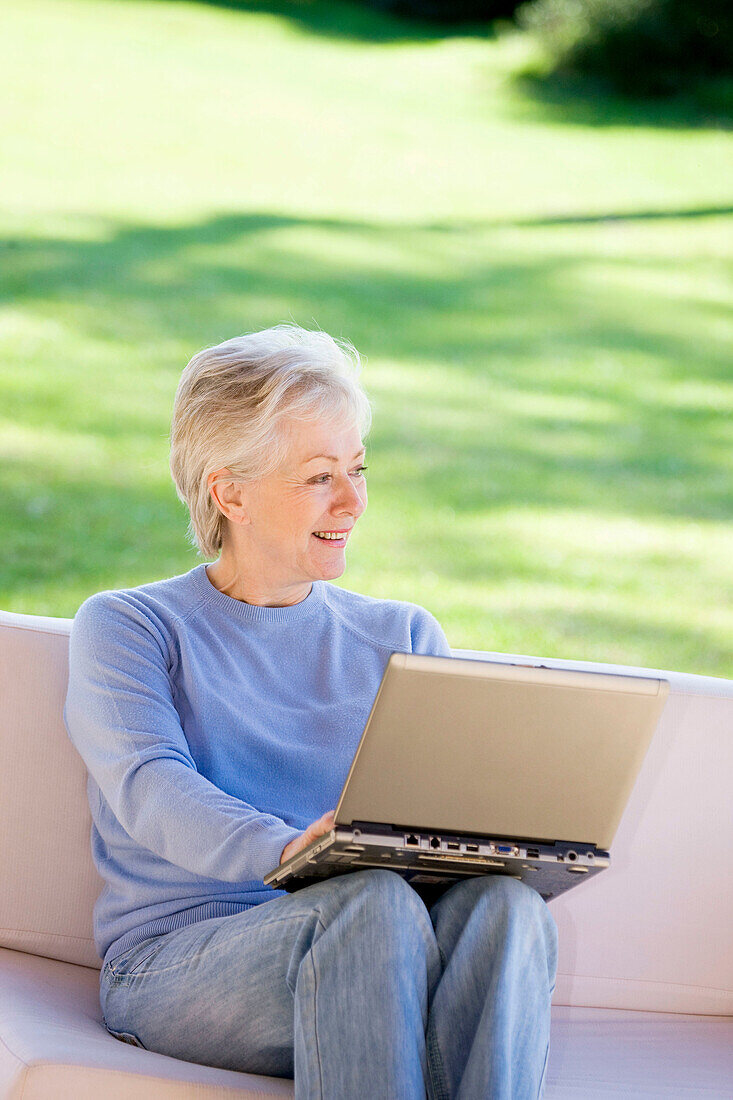 Absorbed, Adult, Adults, Calm, Calmness, Caucasian, Caucasians, Color, Colour, Computer, Computers, Contemporary, Couch, Couches, Daytime, exterior, Female, Garden, Gardens, Gray-haired, Grey hair, Grey haired, Grey hairs, Grey-haired, grin, grinning, Hob