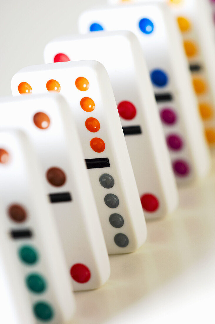 White dominos with multicolored dots stand in a line on white background