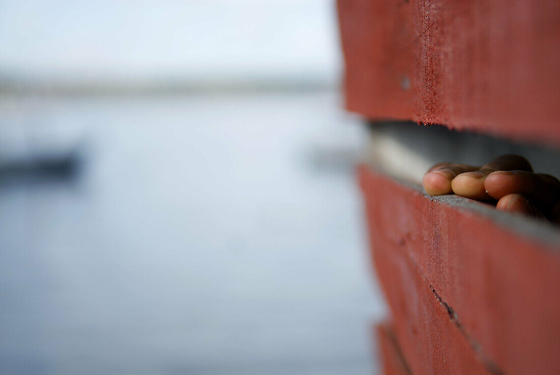 A woman watching through a crack in the wood wall of its house (palafito) in Salvador de Bahia