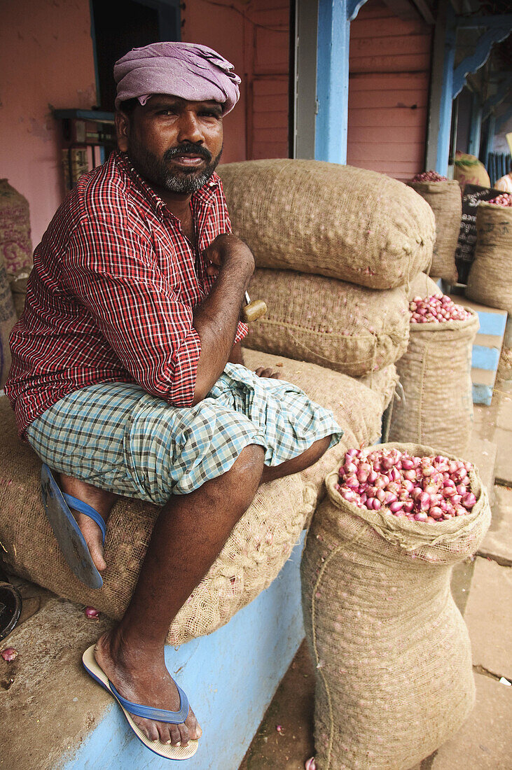 A porter resting on bags of shallots  Kollam,  Kerala,  India