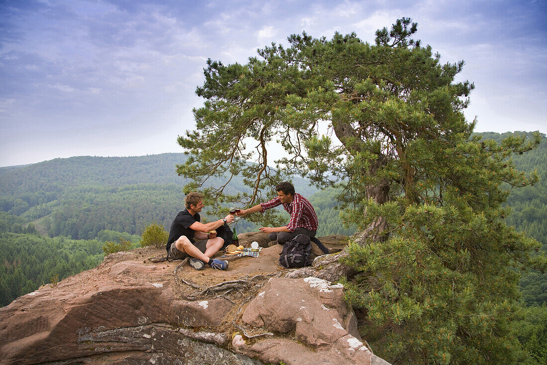 Two men having a picnic on sandston rock, Palatine Forest, Rhineland-Palentine, Germany