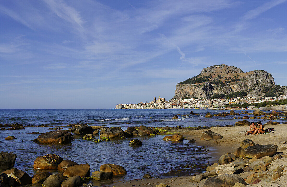 Paar am Strand Blick auf Cefalu mit Rocca di Cefalu, Cefalu, Sizilien, Italien