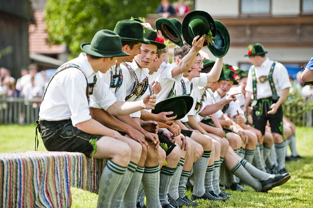 Young men wearing traditional costumes sitting side by side, May Running, Upper Bavaria, Germany