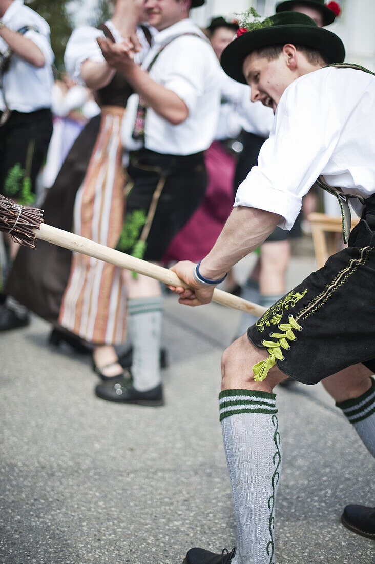 Junger Mann mit Besen, Paare tanzen im Hintergrund, Mailaufen, Antdorf, Oberbayern, Deutschland