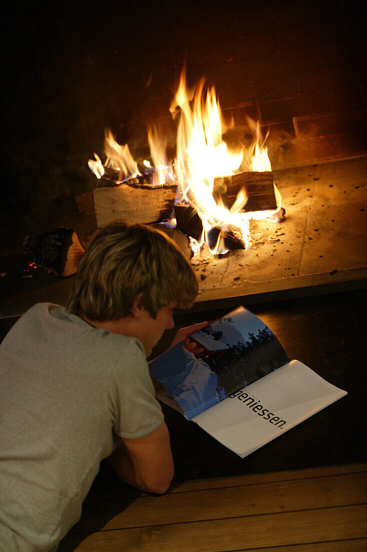 Young man reading in front of open fireplace