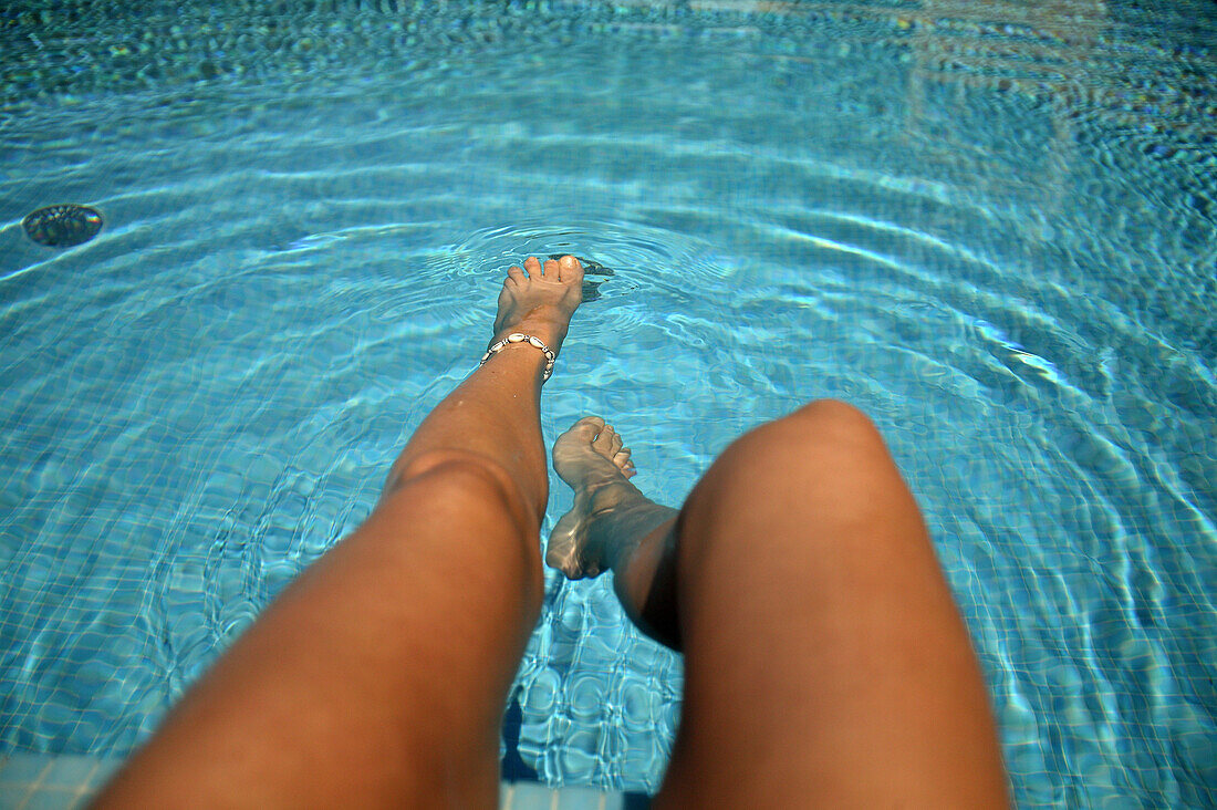 Woman dangling her legs into water, sitting on the edge of a swimming pool