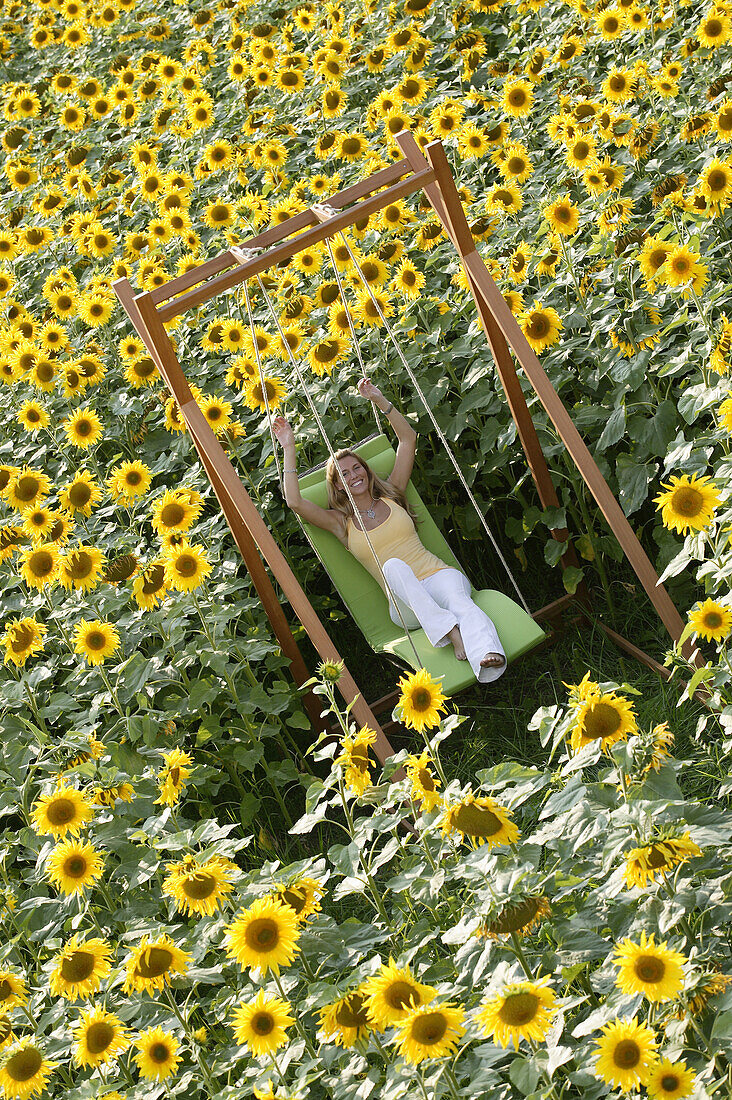 Junge Frau auf Schaukel in Sonnenblumenfeld, Bayern, Deutschland