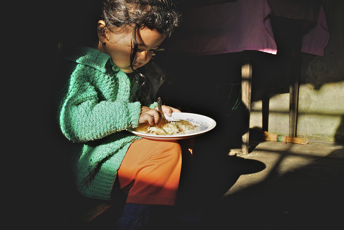 Kleines Mädchen sitzt im Sonnenlicht in der Küche auf Teeplantage Makaibari, Darjeeling, West Bengalen, Indien, Asien