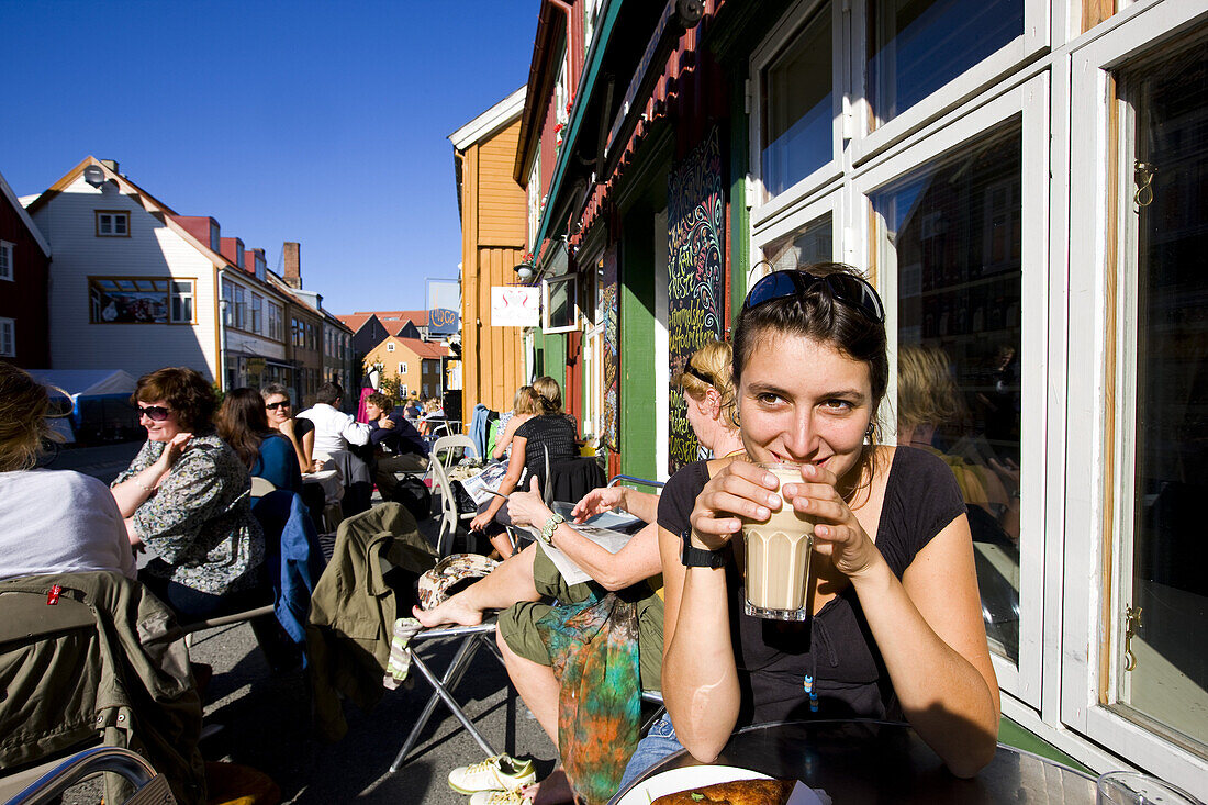 Junge Frau sitzt in einem Straßencafe und trinkt einen Milchkaffee, Stadtviertel Mollenberg, Trondheim, Trondelag, Mittelnorwegen, Norwegen, Skandinavien; Toristin, Europa
