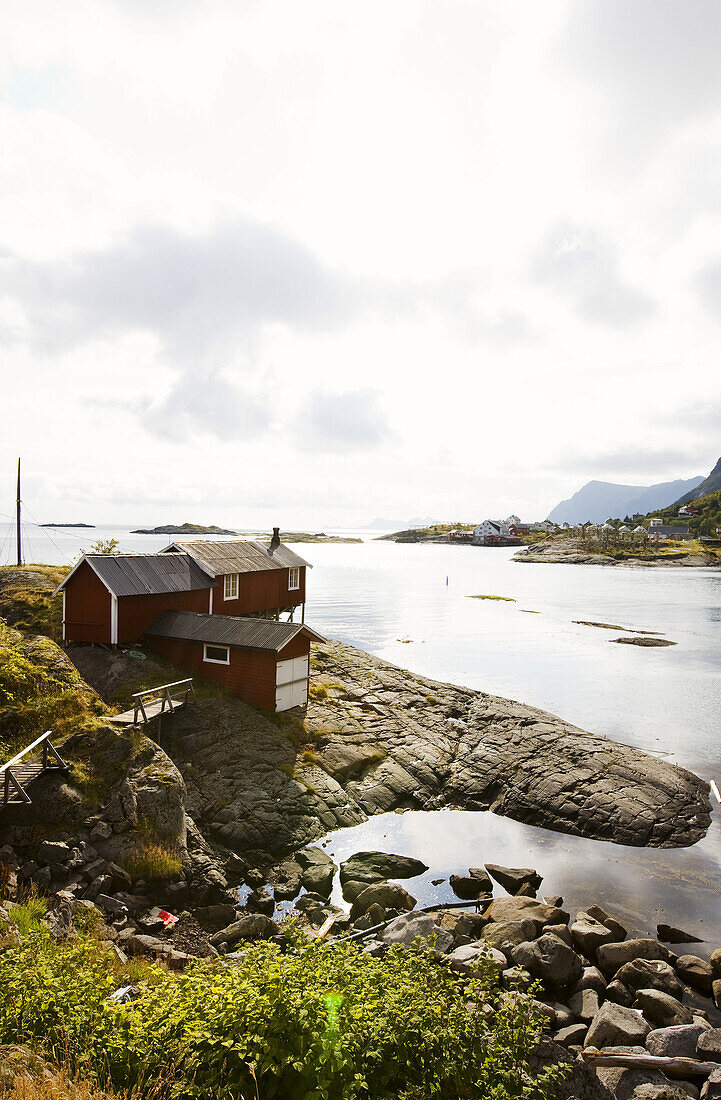 Rote Rorbu Hütte am Wasser in steiniger Küstenlandschaft, Lofoten, Norwegen, Skandinavien; Landschaft, Europa