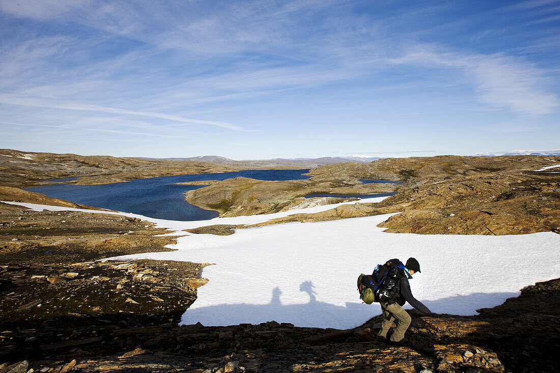 Hiker with rucksack in barren landscape in front of snow field, Saltfjell, Norway, Scandinavia, Europe