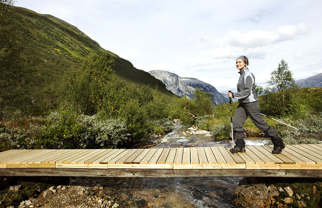 Junge Frau wandert auf einer Holzbrücke über einen Fluß, Rimstigen, Naerofjord, Sogn og Fjordane, Norwegen, Skandinavien, Europa