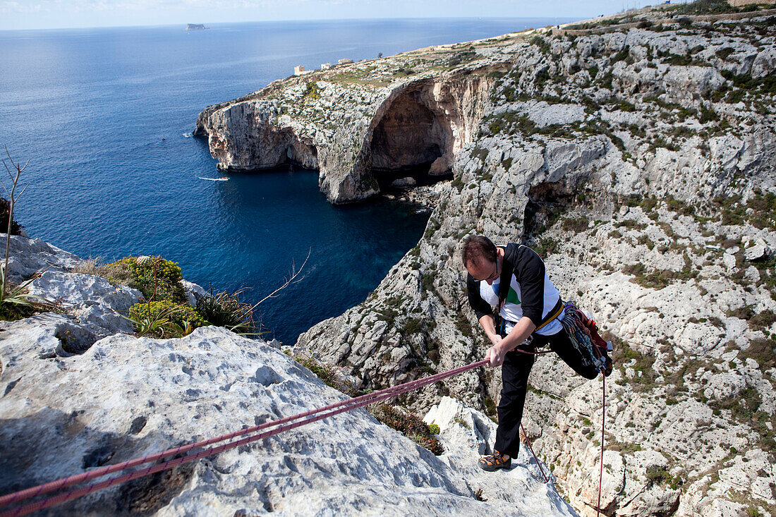 Ein Mann seilt in die Bucht von Zurrieq ab, im Hintergrund die Blue Grotto, Malta, Europa