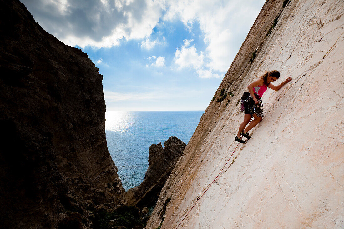 A young woman, a climber, a sportclimber, freeclimber, climbing at Ix-Xaqqa rock face, Malta, She protects with nuts and wires, Europe